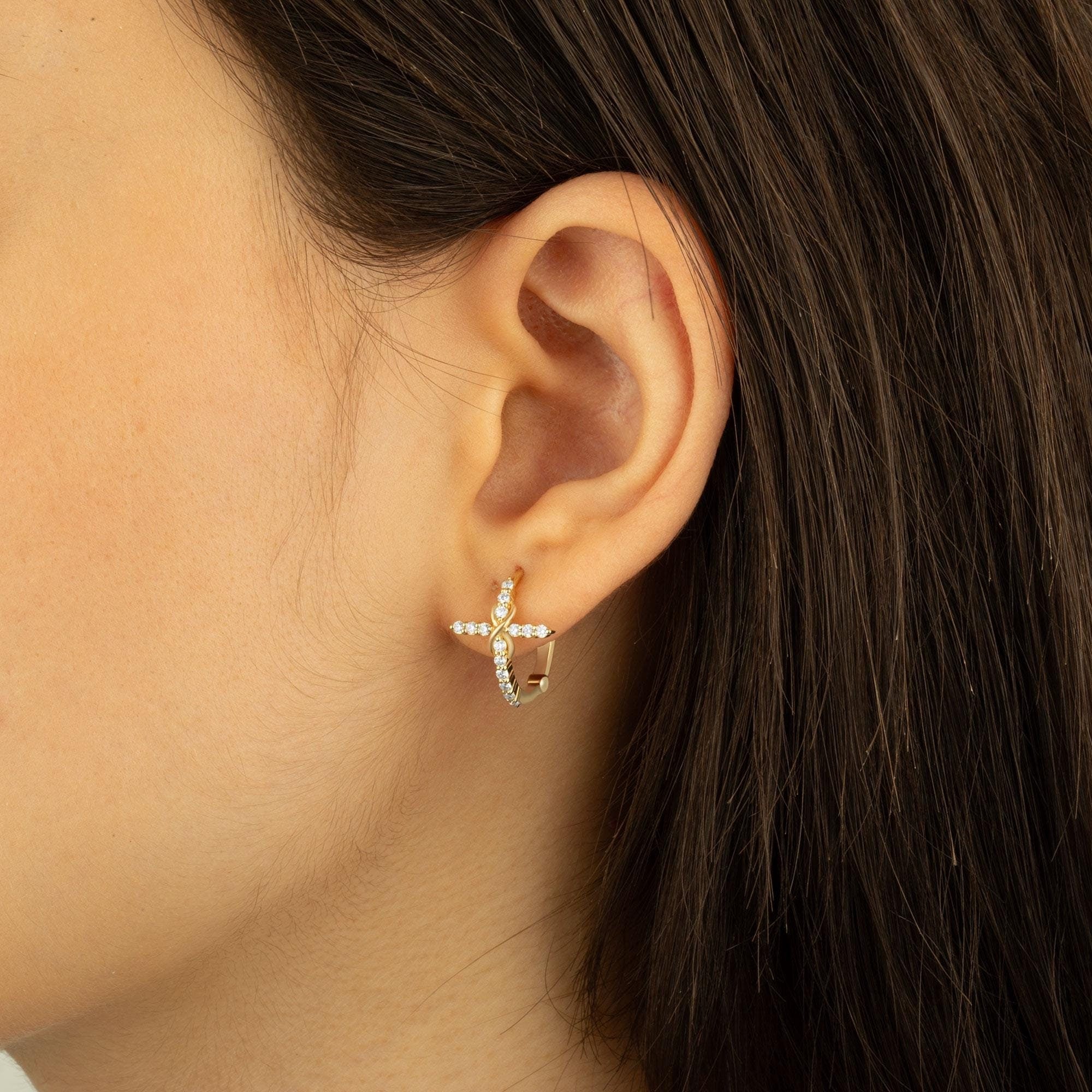 14K gold diamond hoop cross earrings featuring sparkling diamonds and an infinity-inspired cross design, displayed on an ear model.